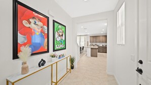 Een hal met twee ingelijste Mario posters, een console tafel met decoratieve objecten, en een uitzicht op een moderne keuken en eetruimte.