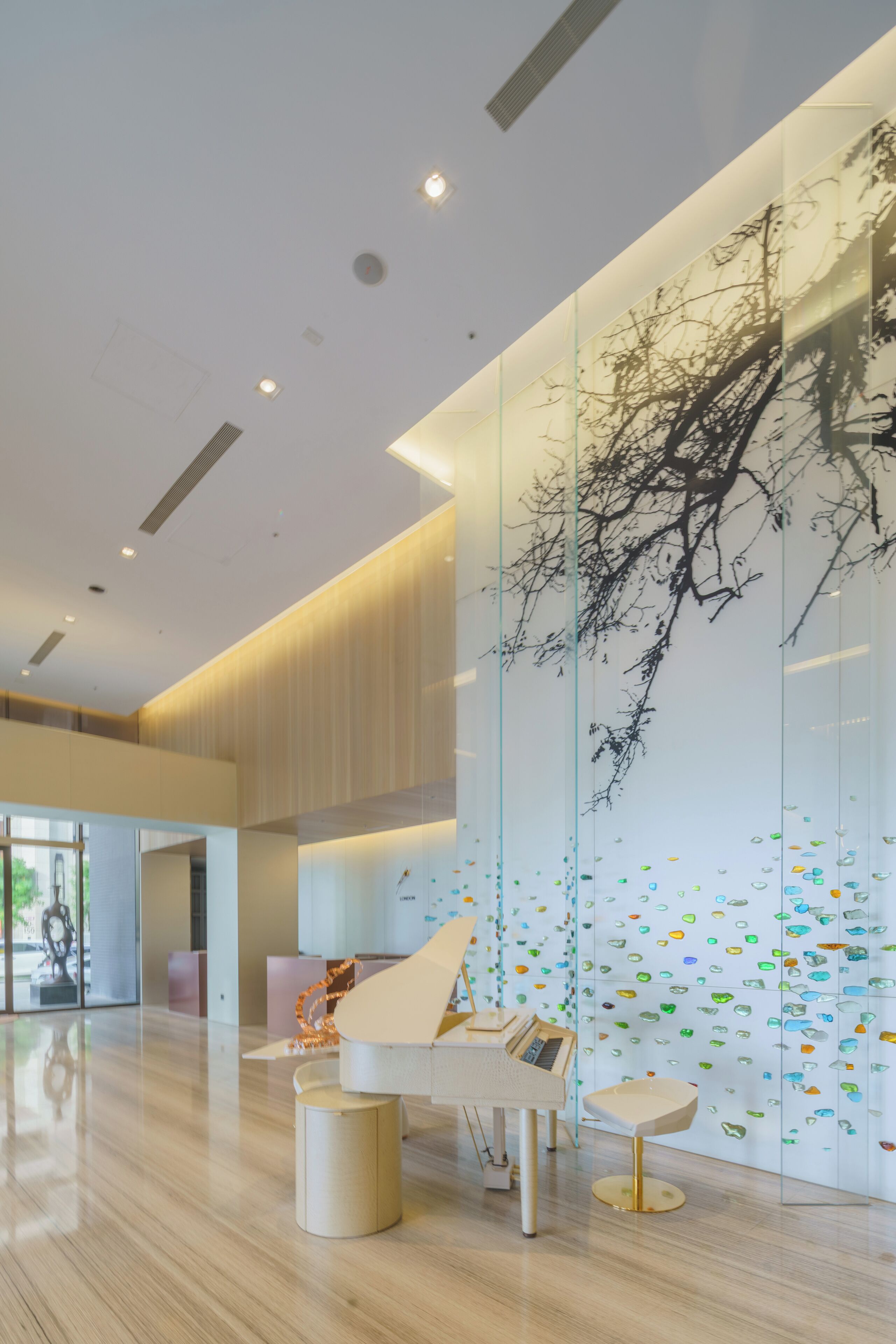 Un intérieur moderne avec un piano à queue, un mur de verre orné d’une fresque représentant un arbre et un plancher en bois.