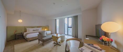 Habitación de hotel con cama, escritorio, silla, mesita de noche, lámpara y ventana con vistas.