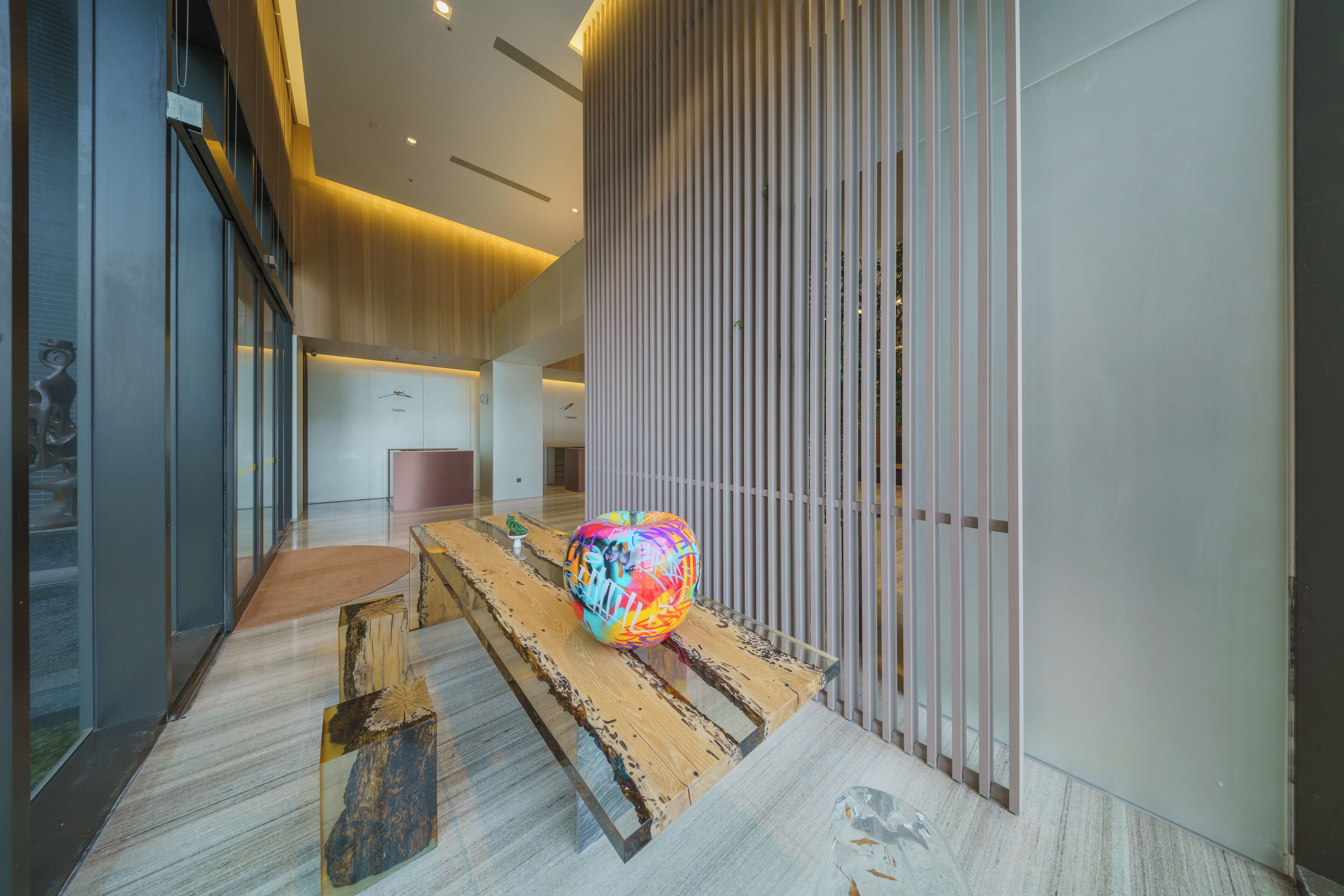 Un interior moderno con un banco de madera, una escultura esférica colorida y un panel de madera vertical.