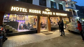 A hotel named "Hotel Kuber Palace N Restaurant" with a modern facade, large windows, and a visible entrance area with people outside. - Hotel Kuber Palace Badrinath (Badrinath)