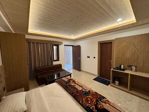 A modern bedroom with a bed, a bench, a wooden wardrobe, and a door leading to a balcony. - Hotel Kuber Palace Badrinath (Badrinath)