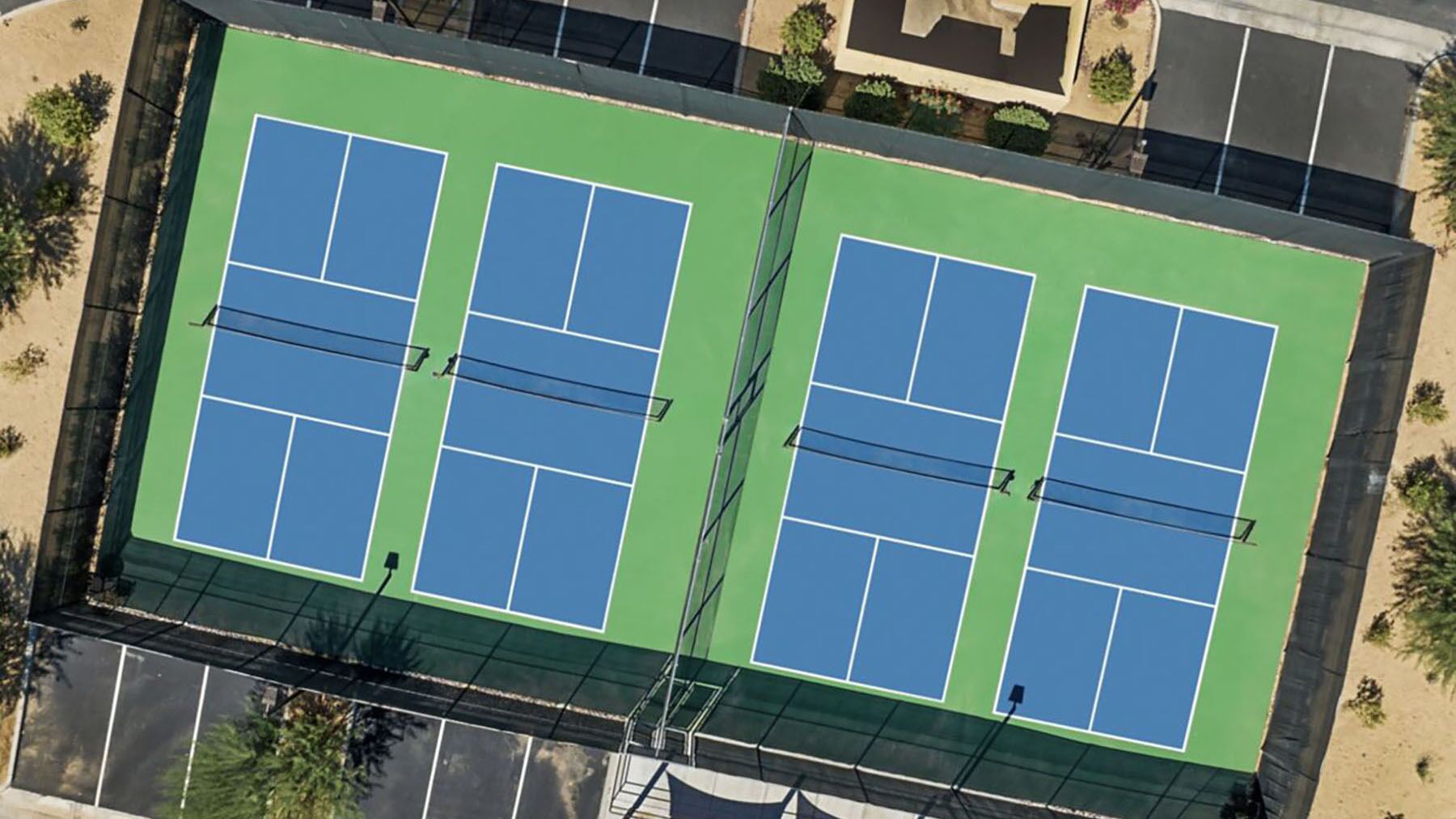 Luchtbeeld van een tennisbaan met vier velden, omgeven door een hek en bomen.
