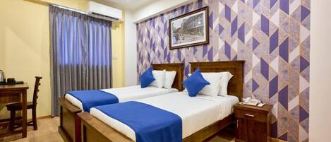 A hotel room with two beds, a wooden desk, a chair, a nightstand, and a patterned wall.