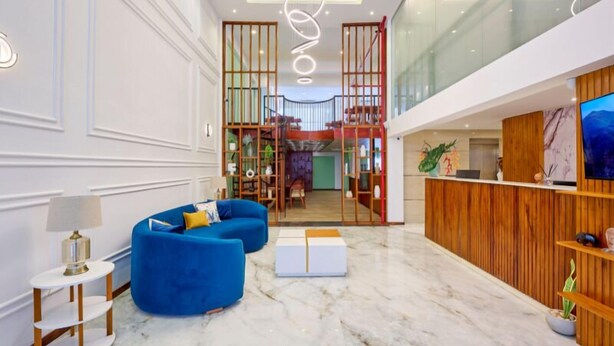 En modern hotellobby med ett marmorgolv, en receptionsdisk och en blå soffa.