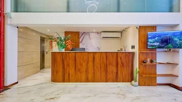 Una moderna recepción con detalles de madera, suelo de mármol y un televisor de pantalla plana grande a la derecha.