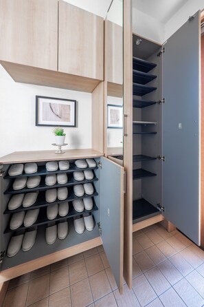 A shoe storage unit with multiple shelves, a small plant, and a framed picture on the wall. - THE VERTEX (Asahikawa)