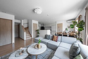 A modern living room with a grey sectional sofa, a round coffee table, and a staircase leading to an upper floor. - THE VERTEX (Asahikawa)