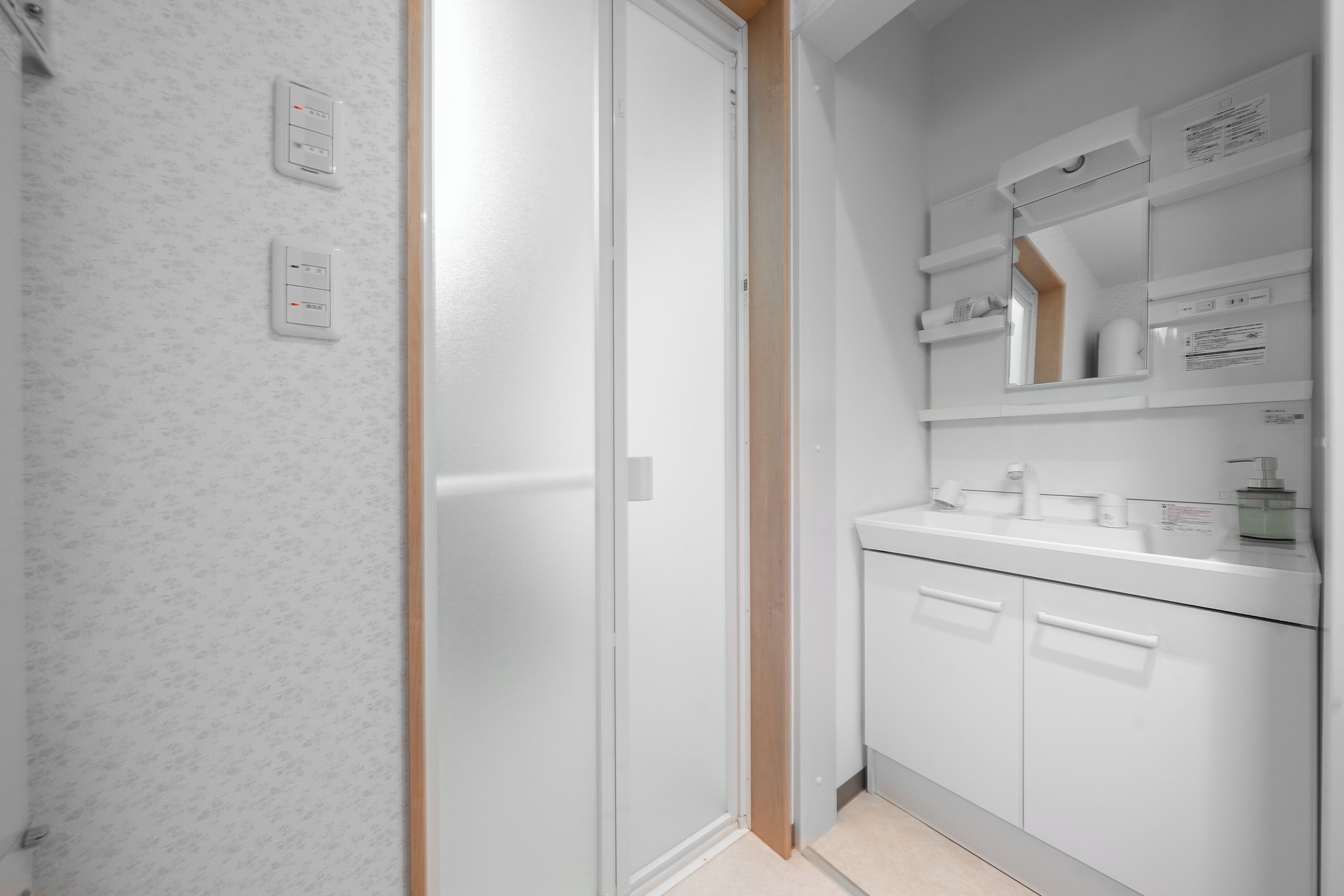 A modern bathroom with a white shower, a glass-enclosed toilet, and a vanity with a mirror and storage.