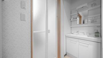 A modern bathroom with a white shower, a glass-enclosed toilet, and a vanity with a mirror and storage.