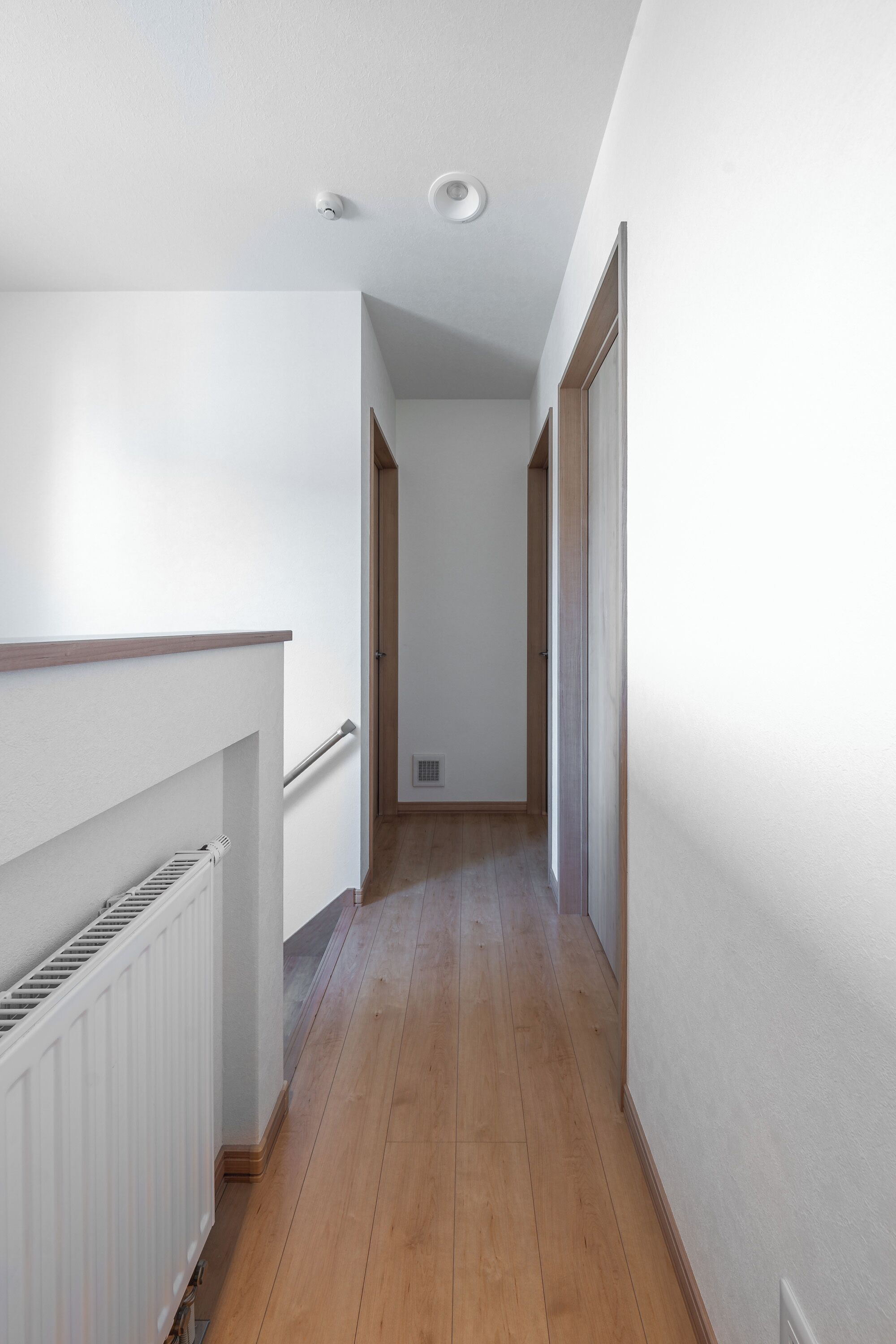 A narrow hallway with wooden flooring, white walls, and a white radiator.