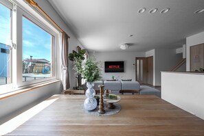 A modern living room with a wooden dining table, a large window, and a flat-screen TV mounted on the wall. - THE VERTEX (Asahikawa)