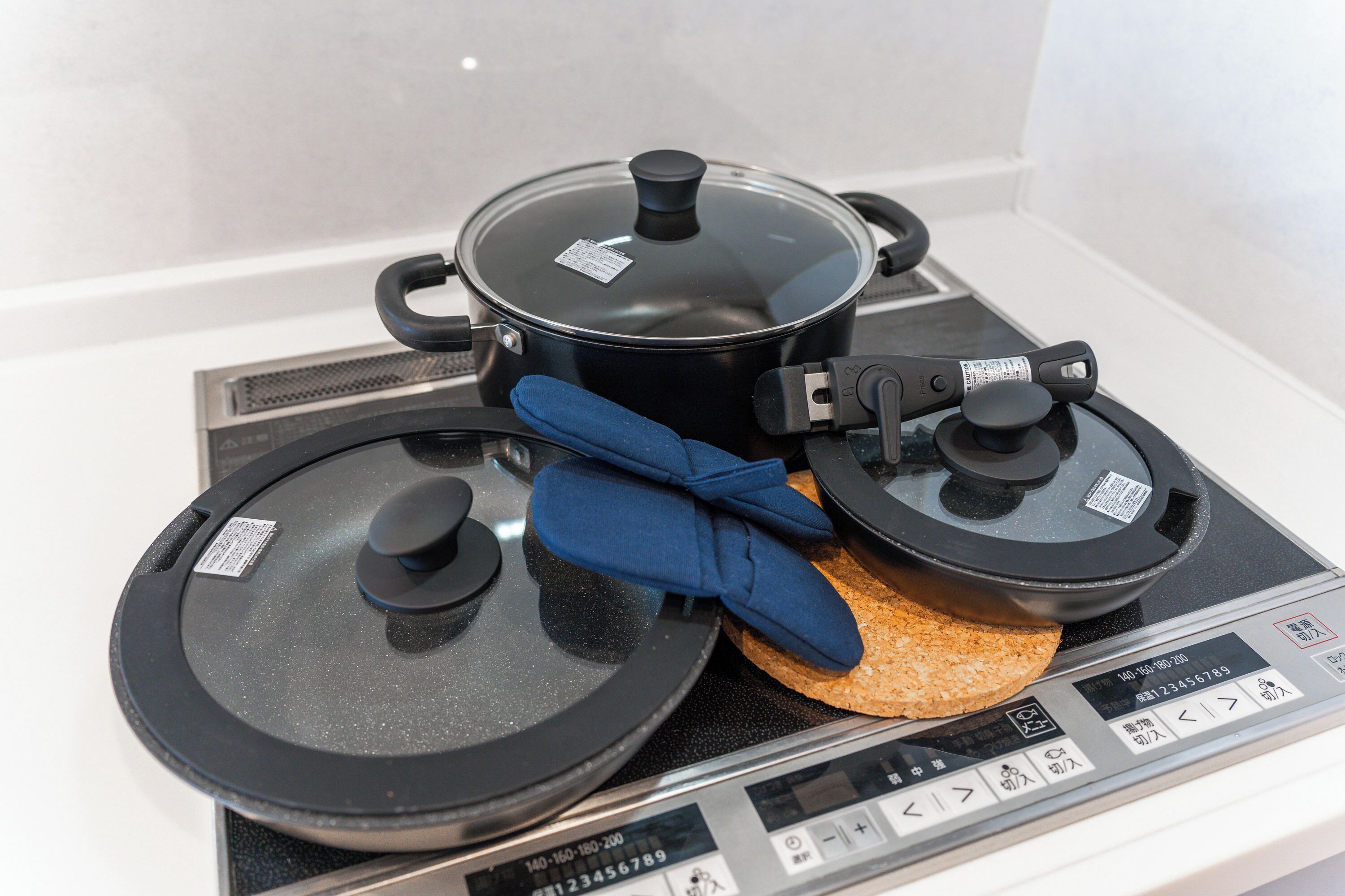Una estufa con una olla y dos tapas, un guante de cocina azul y una hogaza de pan.