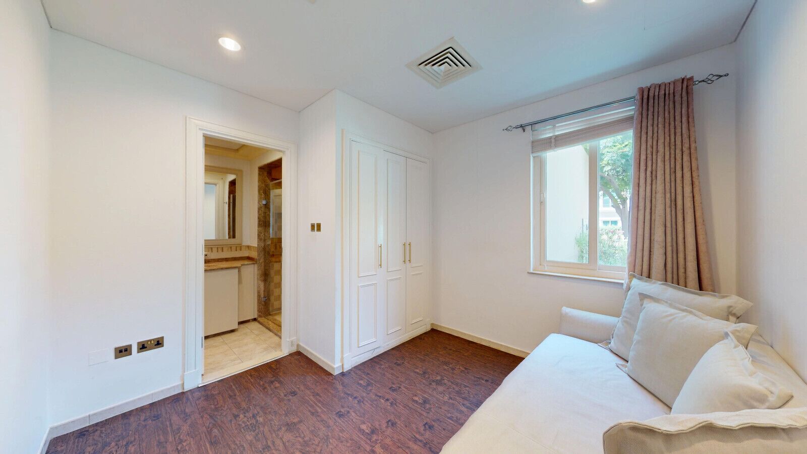 A bedroom with a bed, a window with curtains, a wardrobe, and a bathroom visible through an open door.