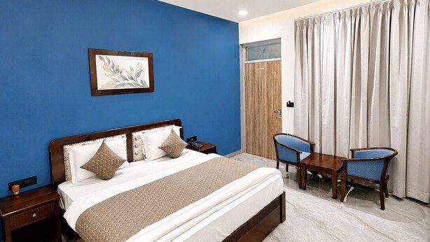 A hotel room with a bed, a desk, two chairs, a ceiling fan, and a window with curtains. - Grand Valley - A boutique Resort in Mount Abu (Mount Abu)