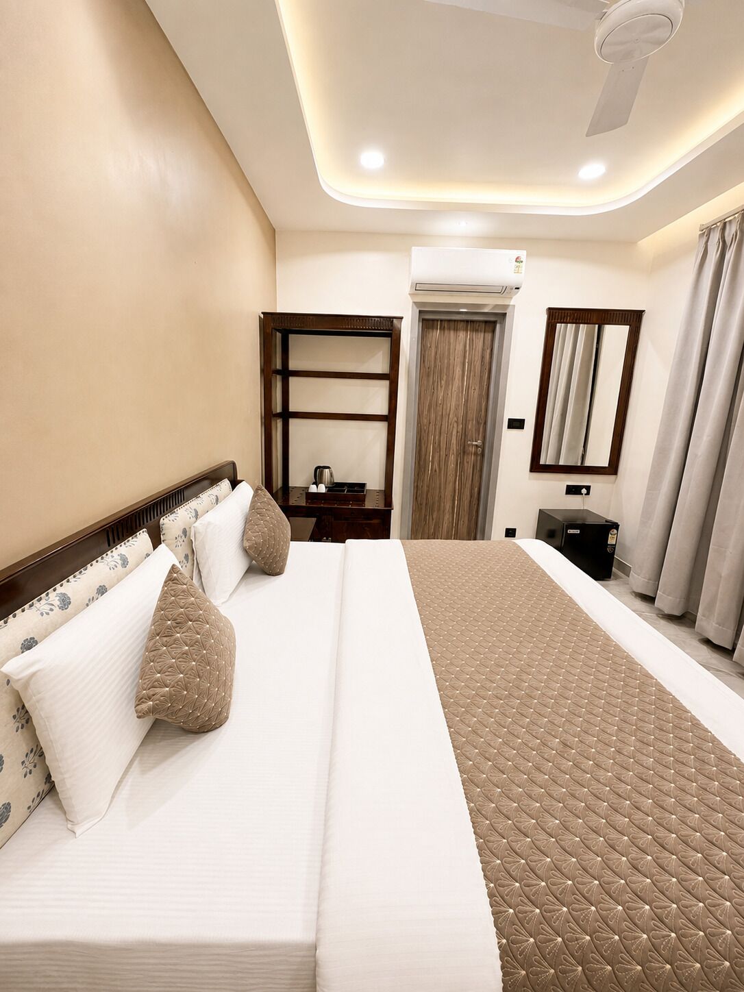A hotel room with a large bed, bedside tables, a wardrobe, a mirror, and an air conditioning unit.