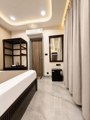 A modern hotel room with a bed, built-in shelving, a small desk, a mirror, and an air conditioning unit. - Grand Valley - A boutique Resort in Mount Abu (Mount Abu)