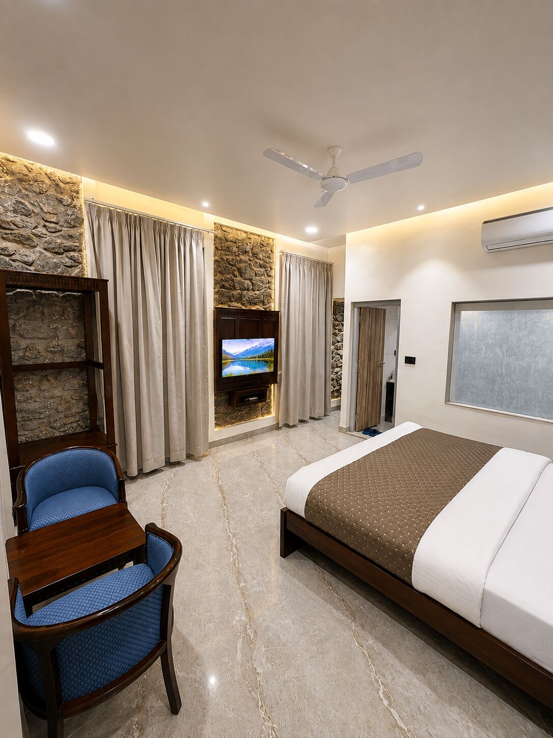 A hotel room with a bed, a TV, a chair, and a ceiling fan.