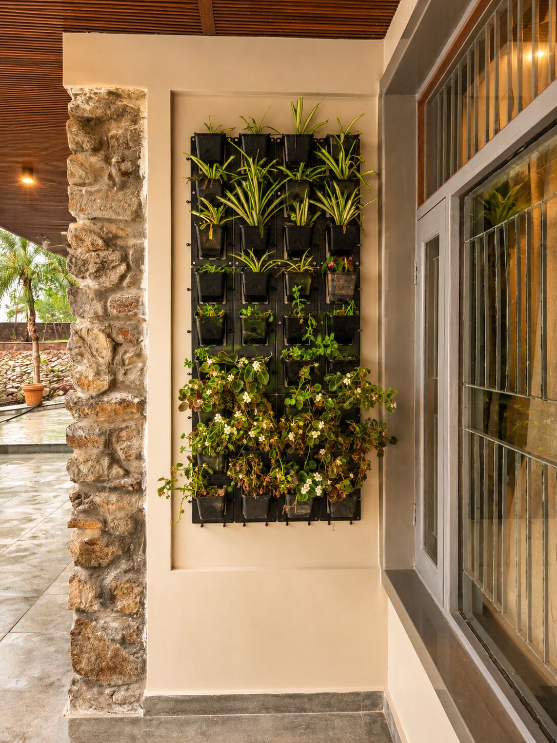 Un muro vertical cubierto de plantas, un pilar de piedra y una ventana con rejas.