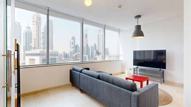 A modern living room with a large window, a grey sofa, a red table, a TV, and a pendant light.
