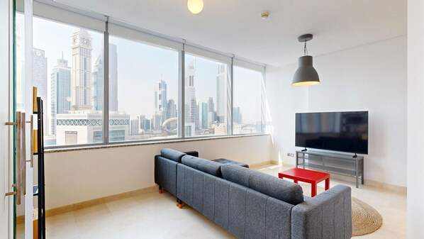 A modern living room with a large window, a grey sofa, a red table, a TV, and a pendant light.