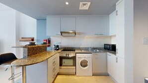 A compact kitchen with a granite countertop, stainless steel appliances, and a built-in washer and dryer.