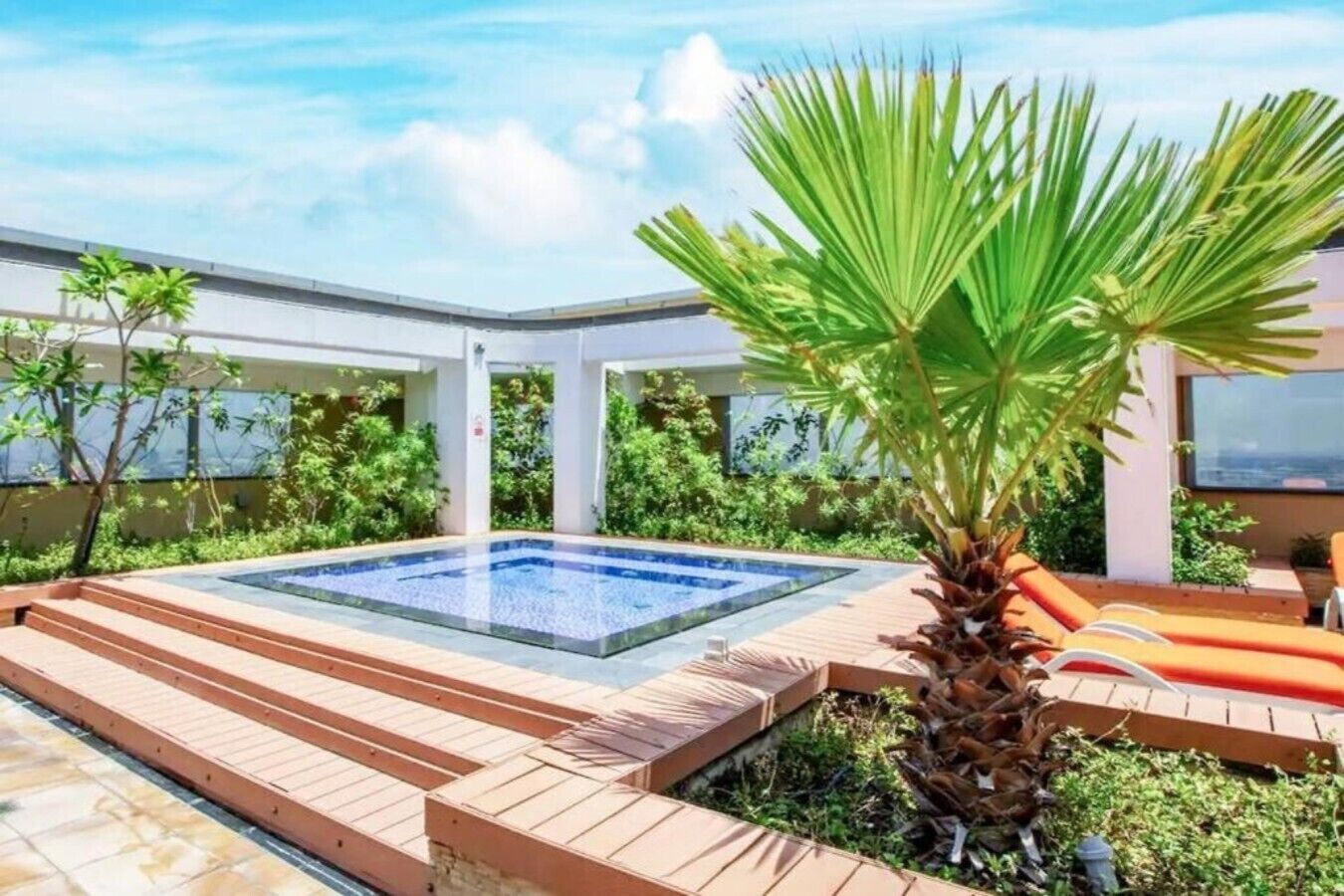 A modern outdoor pool area with a hot tub, wooden deck, and lush greenery.