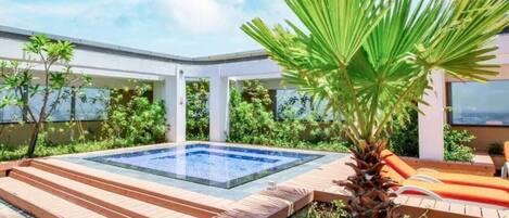 A modern outdoor pool area with a hot tub, wooden deck, and lush greenery.