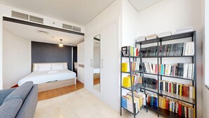 A modern bedroom with a bed, a grey sofa, and a bookshelf filled with books.