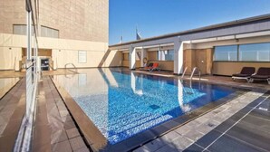 A rooftop swimming pool with clear blue water, surrounded by lounge chairs and a modern building with large windows.