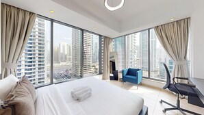 Una habitación de hotel moderna con una cama grande, un escritorio, una silla y vistas de la ciudad a través de amplias ventanas.