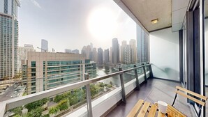 Un balcón con vista a la ciudad, barandilla de vidrio y banco de madera.