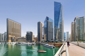 Un paisaje urbano con modernos rascacielos, un puerto deportivo con barcos y un paseo peatonal.