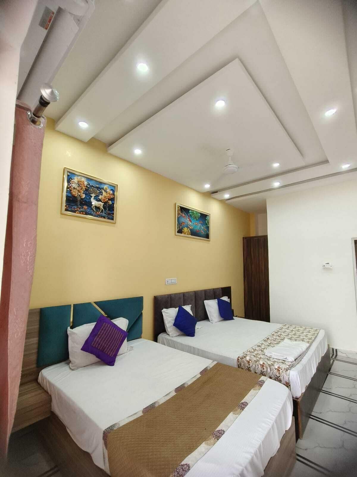 A hotel room with two beds, a ceiling fan, recessed lighting, and two wall-mounted paintings.