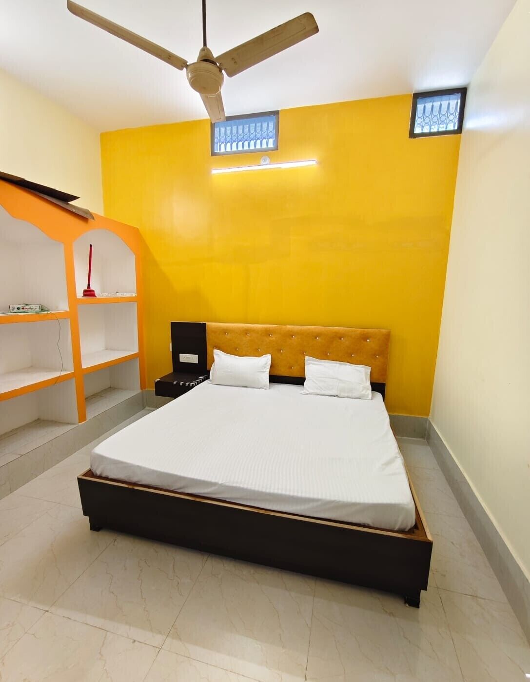 Une chambre à coucher avec un lit, un ventilateur de plafond et une étagère.