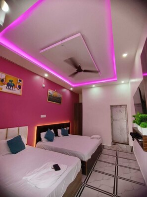 Una camera d'albergo moderna con due letti, una ventola a soffitto e illuminazione ambientale rosa.