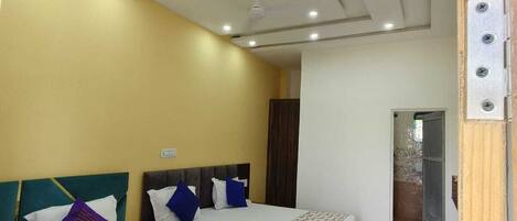 Habitación de hotel con dos camas, ventilador de techo, iluminación empotrada y piso de baldosas.