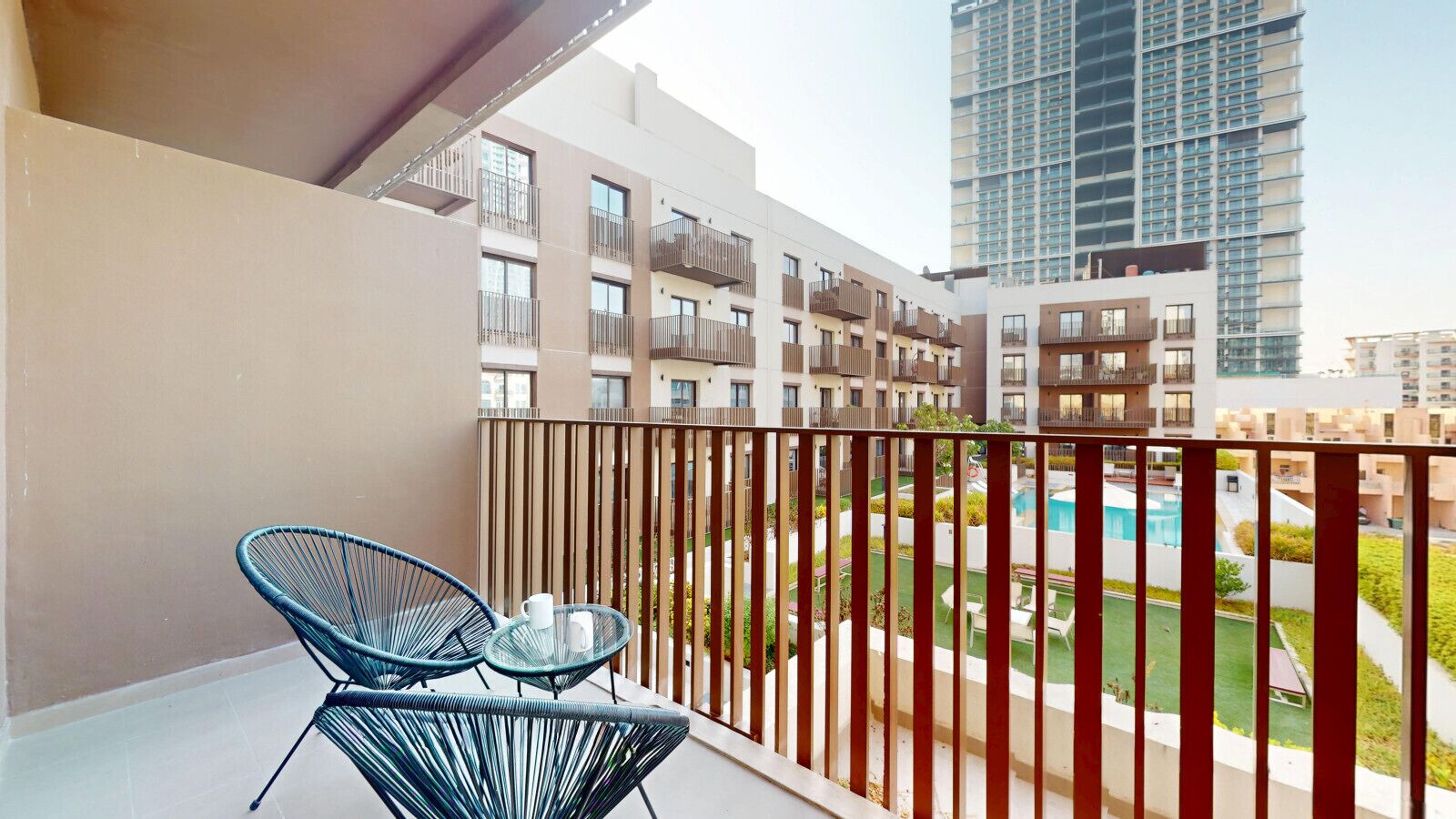 A balcony with two chairs and a table, overlooking a pool and residential buildings.