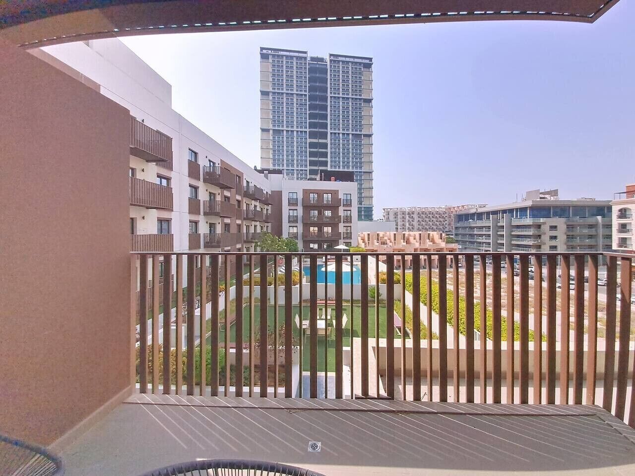 A balcony with a view of a swimming pool, adjacent buildings, and a tall skyscraper in the background.