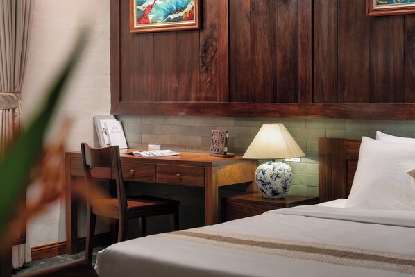 Habitación de hotel con cama, escritorio con lámpara, silla y un cuadro en la pared.