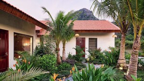 A building with a red-tiled roof, surrounded by lush tropical plants and palm trees. - The Greenary Garden (Ninh Binh)