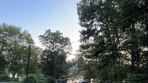 Un foyer extérieur avec deux chaises, entouré d’arbres et d’une haie, avec une voiture garée au loin.