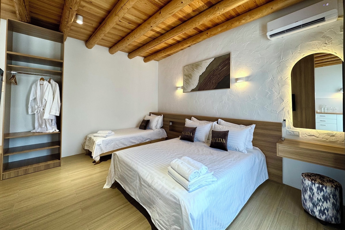 A hotel room with two beds, a wooden ceiling, a wardrobe, and a bathroom with a mirror and sink.