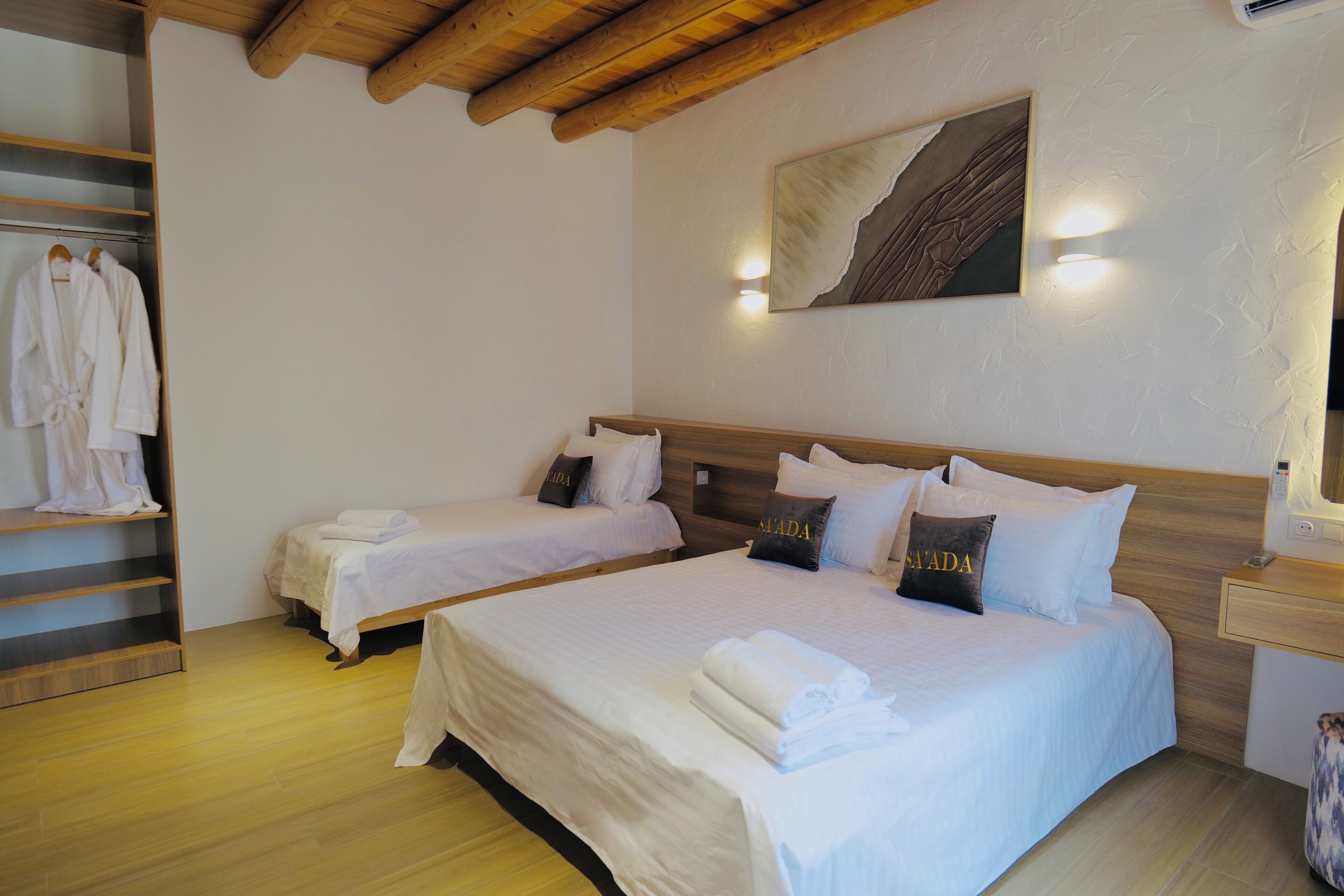 A hotel room with two beds, a wooden ceiling, a wall-mounted artwork, and a side table with a lamp.