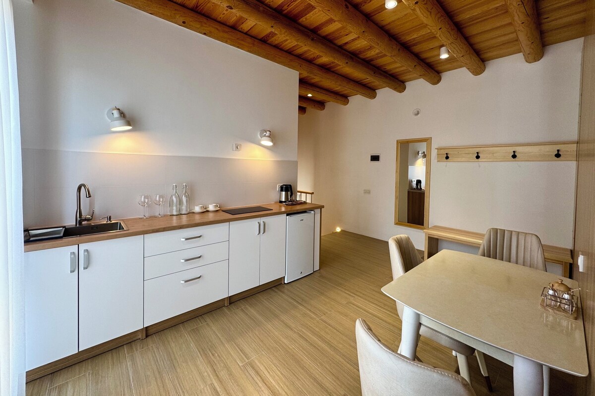 A modern kitchen with wooden beams, white cabinets, and a dining area with a table and chairs.