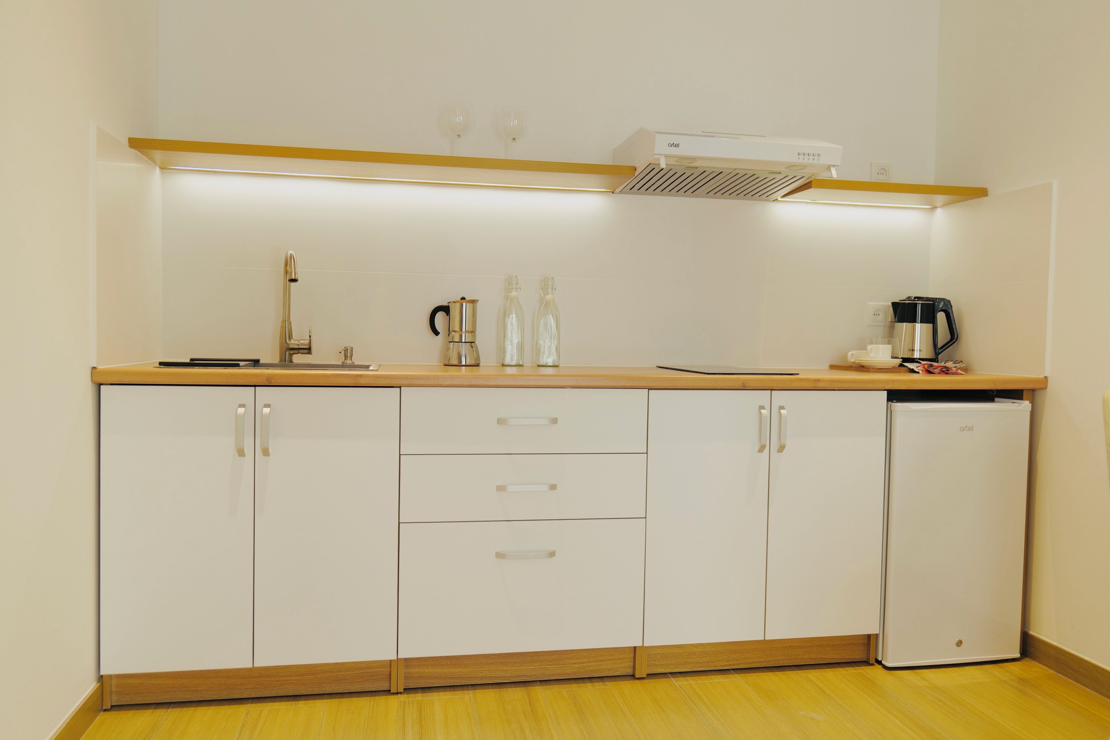 Une cuisine de taille réduite avec des meubles blancs, un plan de travail en bois, une machine à café et un réfrigérateur compact.