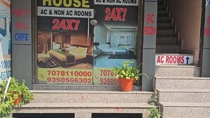L’entrée d’un hôtel, avec une enseigne indiquant la présence de chambres climatisées et de chambres non climatisées, une disponibilité 24 heures sur 24, 7 jours sur 7, et des numéros de téléphone à contacter.