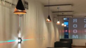 A modern interior with black leather booths, pendant lighting, and a projection screen displaying "ROOM". - Town house cafe and hotel (Kurukshetra)