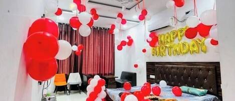 A room with a bed, a desk, and a chair. There are balloons and a 'Happy Birthday' sign.