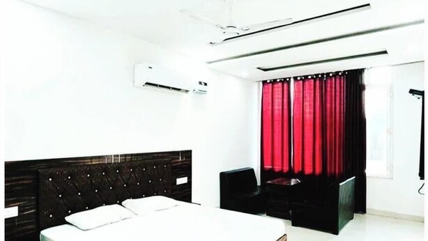 A modern bedroom with a large bed, a dark headboard, a red curtain, and a ceiling fan. - Town house cafe and hotel (Kurukshetra)